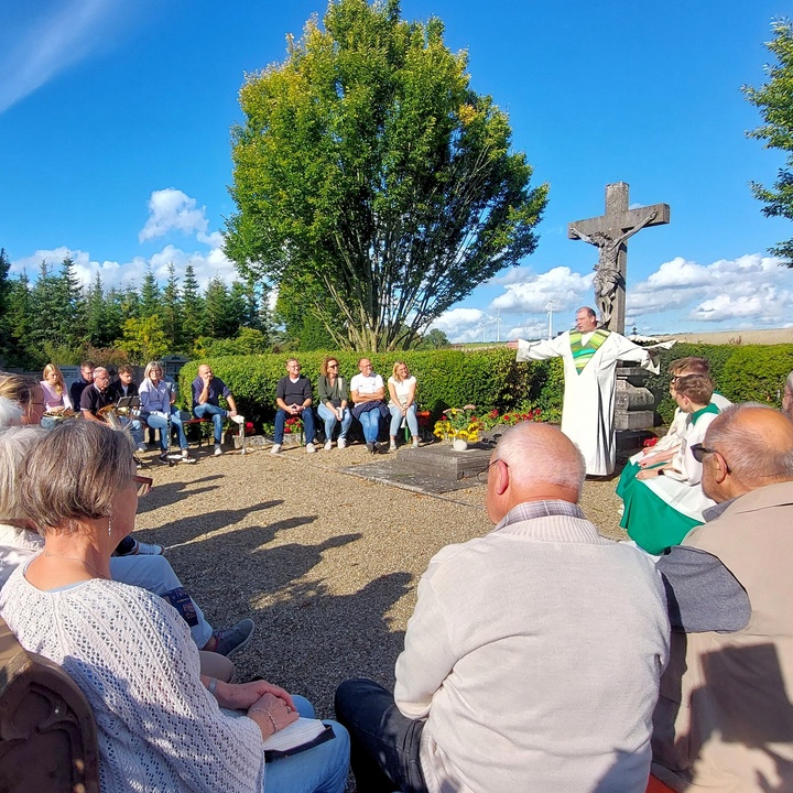 In einem Kreis sitzen Menschen um das Kreuz im Friedhof.